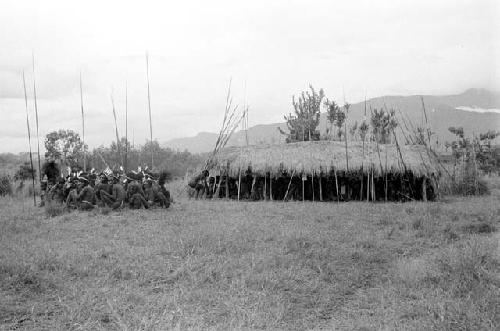 Men sit next to and under an oléa on the Liberek, their spears around them