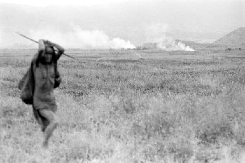 A woman in a field; fires burn in the distance