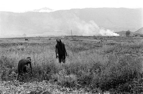 Women in a field; fires burn in the distance