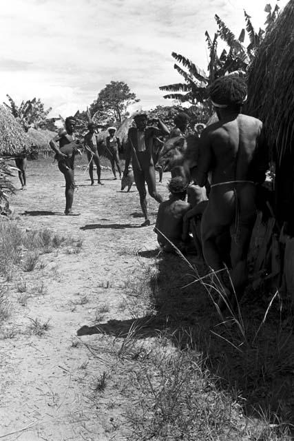 man stands holding a pig, beyond another man holding a pig waiting its turn to be killed