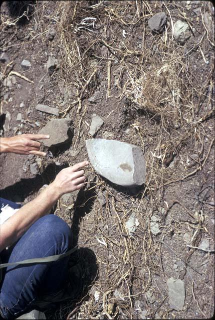 Close-up of someone pointing at a rock at the site of Pinit (U2343), a hill-top fort