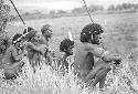 Men sitting in grass with poles