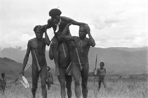 Four men walking, one with a man on his shoulders