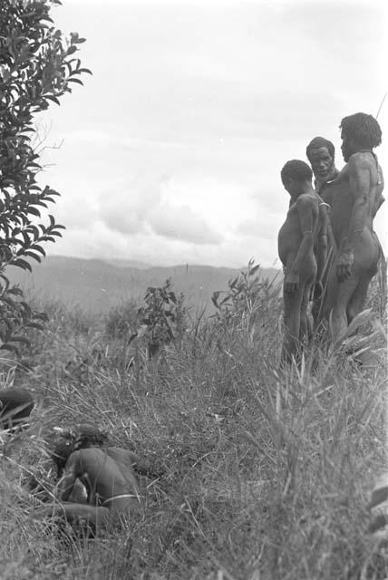 Men standing in tall grass over men crouched in grass