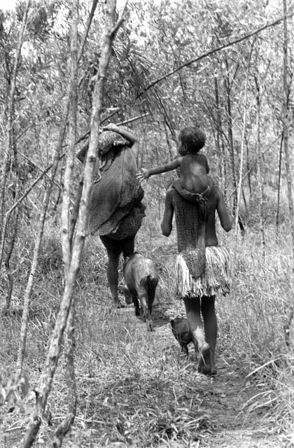 Boy carrying toddler  following a man