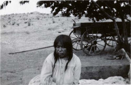 Woman seated on ground, wagon lies behind her