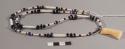 Necklace of long bone beads; black stone chip beads with sparkles; off-white and black opaque glass beads; large clear purple glass beads; small purple crystal beads; ivory pendant with Cape Alitak petroglyph design
