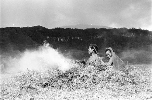 Two women in fields; smoking by a fire; the eastern mountain wall behind them