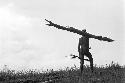 Man walking along outside of Homoak with a large log on shoulder