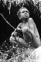 Yegé Abu sitting on a rock with a hoop and spear