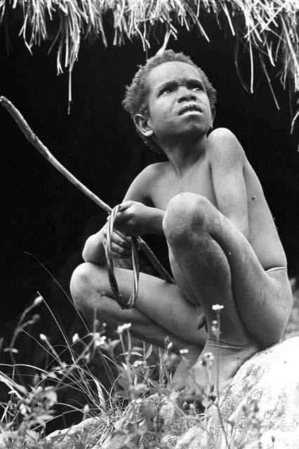 Yegé Abu sitting on a rock with a hoop and spear