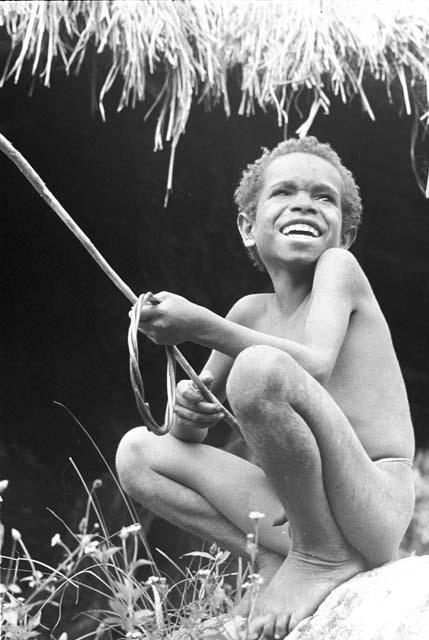 Yegé Abu sitting on a rock with a hoop and spear