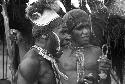 Tegé Warek and Mu; Tegé Warek in an inamossi and Mu with feathers on his head dress; they talk near the oléa at Puakoloba