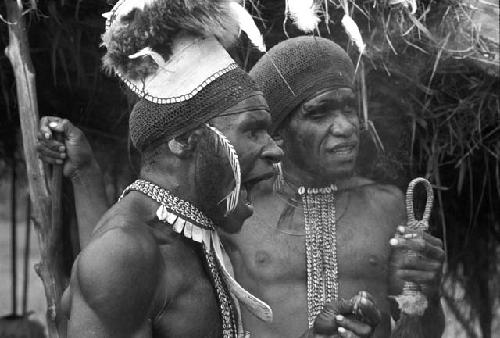 Tegé Warek and Mu; Tegé Warek in an inamossi and Mu with feathers on his head dress; they talk near the oléa at Puakoloba