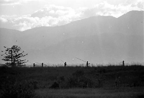 Men walking home; silhouetted on a ridge as they walk past