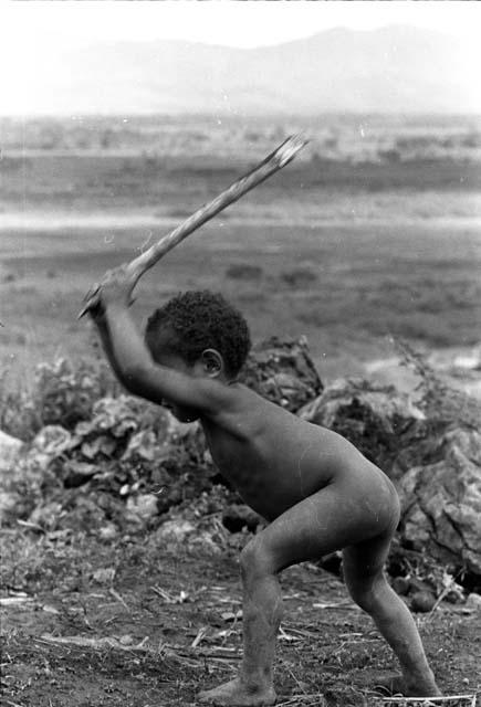 child beats a stick on the ground