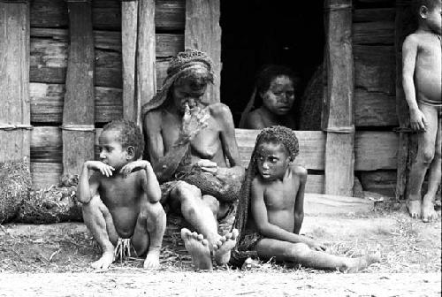 Woman mourning and 2 little girls sitting near her; a woman's face in the doorway of the hunu