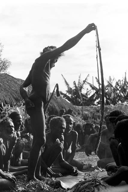 A man holds up a nyeraken aré to hand out at the funeral for the old woman