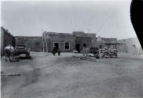 Horse and wagons, two people, stack of stones in village plaza