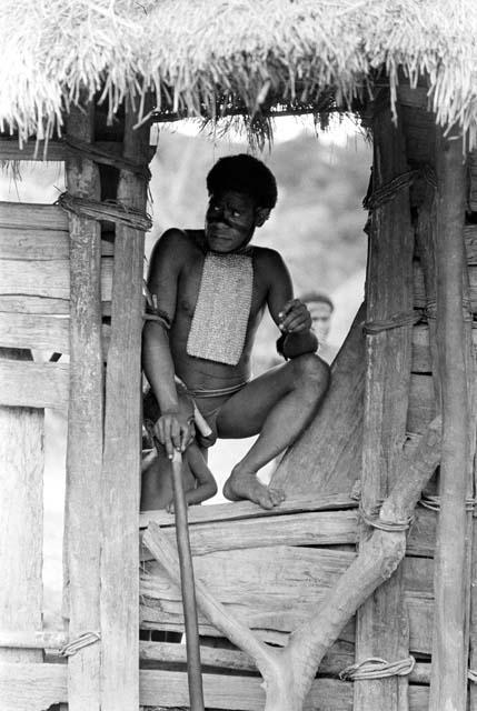 Yegé Asuk standing in the doorway of Homaklep, he's carrying a club