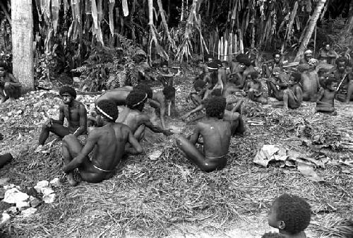 Men and boys sit waiting for the hakse to be completed and finished cooking