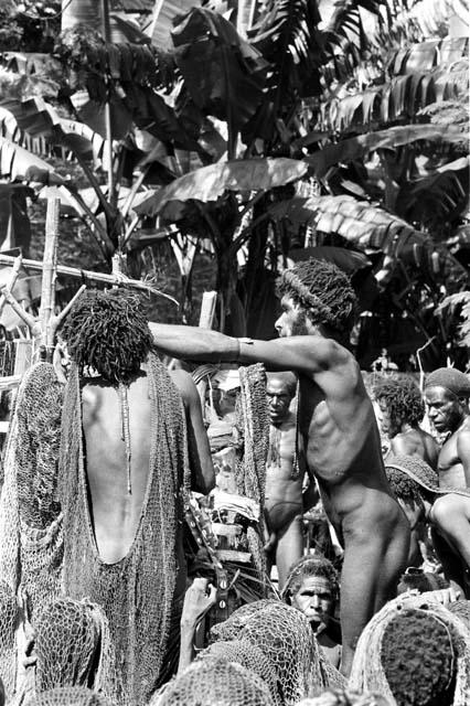 A man arranges something on Weaké; over heads of women; fixing cowrie shells