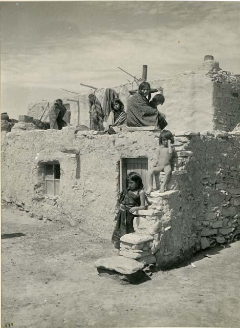 Hopi woman and children sitting and standing on pueblo roof and steps at Oraibe