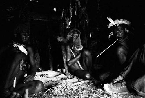 3 men seated in honai; Michael Rockefeller's feet and legs in right hand half of frame