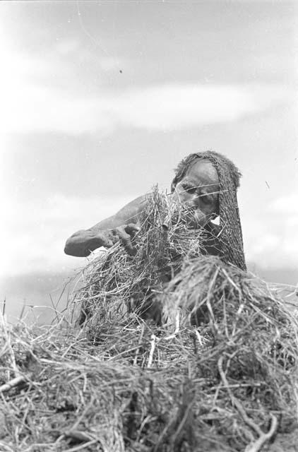 A woman trying to get some cinders in a grass bundle started to burn - to burn trash in the fields