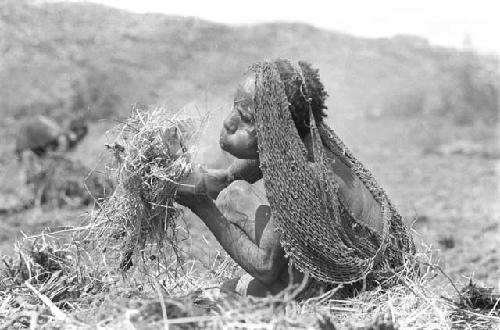 A woman trying to get some cinders in a grass bundle started to burn - to burn trash in the fields