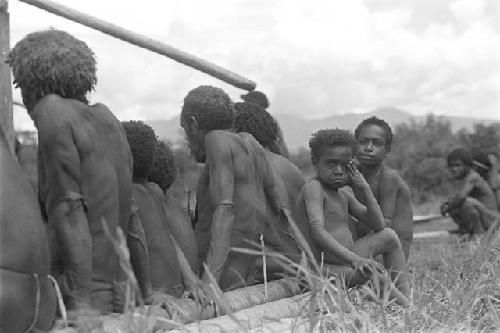 Tukom in a group with men sitting, watching as the building is constructed