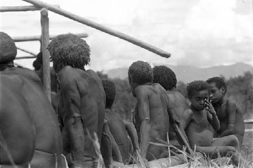 Tukom in a group with men sitting, watching as the building is constructed