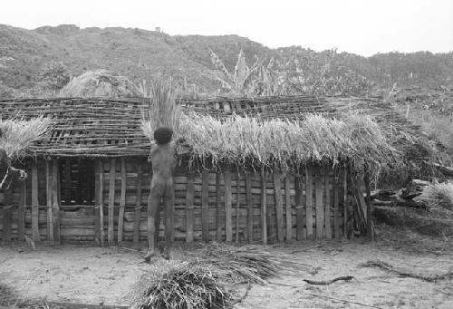 Apeori and another man begin the thatching on the roof of the new hunu in Abukulmo