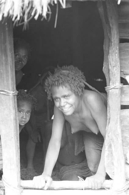 Two women and child look out of doorway of hunu