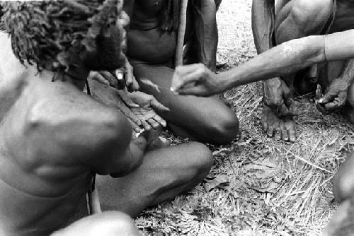 Men being 'cleaned'; this is Sue samilek; feather is being brushed over the hands of men who have something to do with this dead body