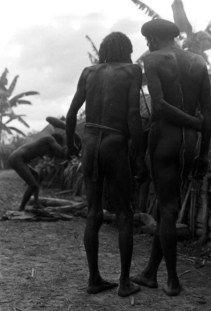 Two men talking; in the distance wood is being split with a huge stone axe