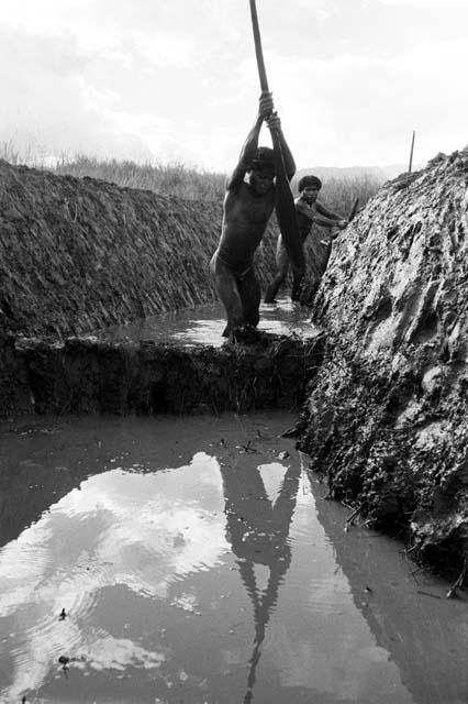 Down in a ditch; man working clearing it of the trash in it