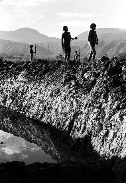 Ditch and ne mt. wall; men standing with their digging tools on the bank