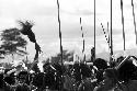 Group of warriors singing; one lifts a sué laré in the air