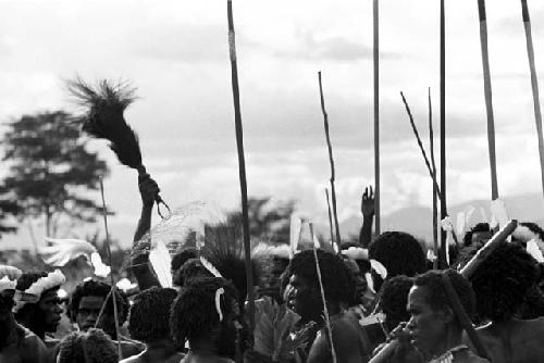 Group of warriors singing; one lifts a sué laré in the air