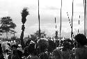 Group of warriors singing; one lifts a sué laré in the air