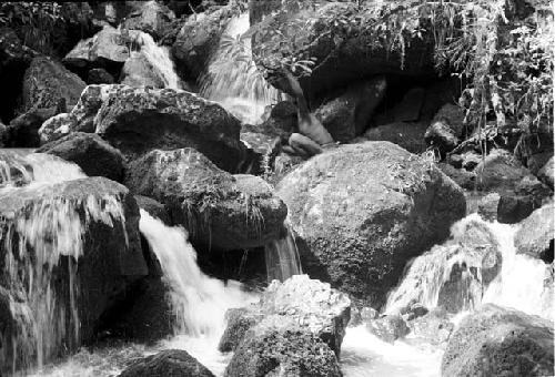 Water rushes over the rock; man sits to drink