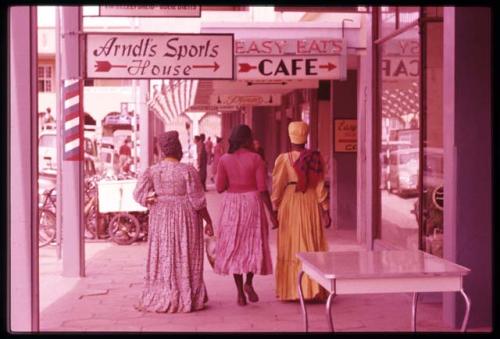 Three women walking down the street under Kaiserstrasse arcade, view from behind