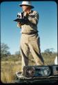 Expedition, Personnel: Laurence Marshall standing on the top of an expedition truck holding a Polaroid camera