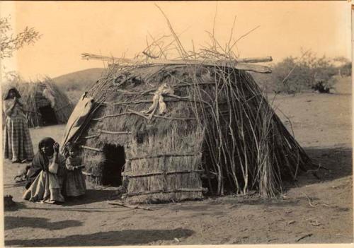 Two women and a small girl standing next to hut