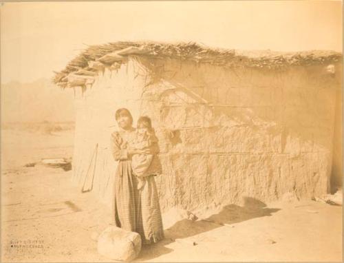 Woman and child standing in front of adobe house