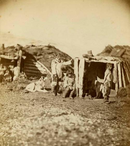 Inuit woman and children in front of house