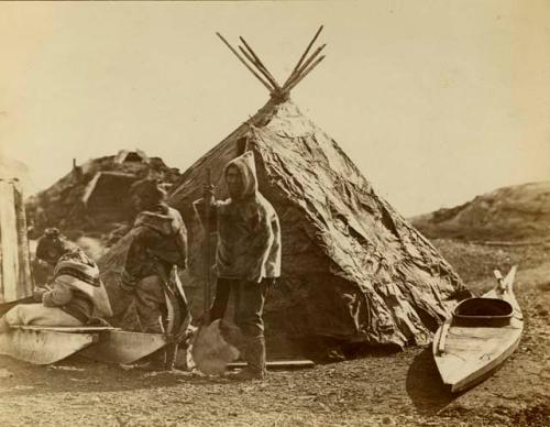 Inuit man and two women in front of tent, with kayak next to it