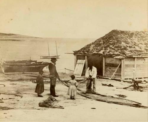 Two Inuit men with net, and two girls near plank shed