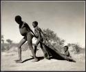 "Pulling on Kaross / Pulling on Gemsbok Horns / Carrying on Kaross "Airplane".": Two boys pulling "Little /Qui" on a kaross, a game they frequently played (print is a cropped image)